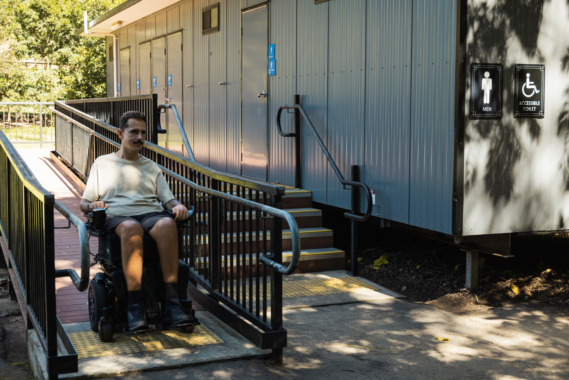 A man in a powerchair on the ramp beside the accessible toilets, with accessible toilet signage on the wall.